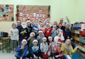 Uczniowie klasy 2a pozują do zdjęcia w mikołajkowych czapkach