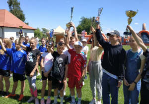 Uczniowie cieszą się po wygranej i wznoszą do góry zdobyty puchar.