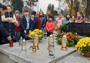 Uczniowie palą znicze na grobie pierwszego dyrektora szkoły.