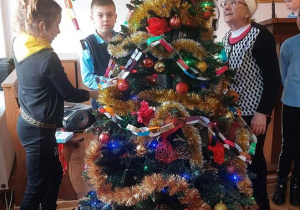 Uczniowie wraz z pensjonariuszami ubierają choinkę.