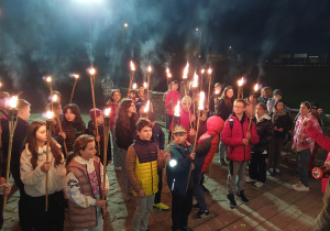 Zdjęcie uczniów trzymających w nocy pochodnie.
