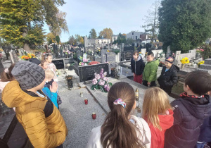 Uczniowie palą znicze na grobie pierwszego dyrektora szkoły.