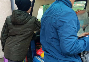 Uczniowie pakują zebrane rzeczy do bagażnika auta.