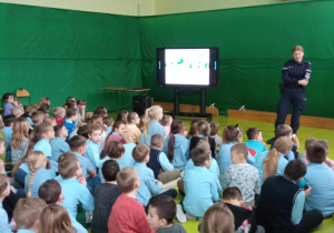 Uczniowie oglądają film edukacyjny i słuchają prelekcji policjanta.