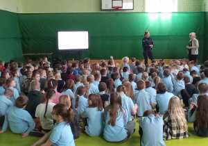 Uczniowie oglądają film edukacyjny i słuchają prelekcji policjanta.