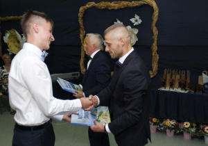 Dyrektor wręcza uczniowi nagrodę.